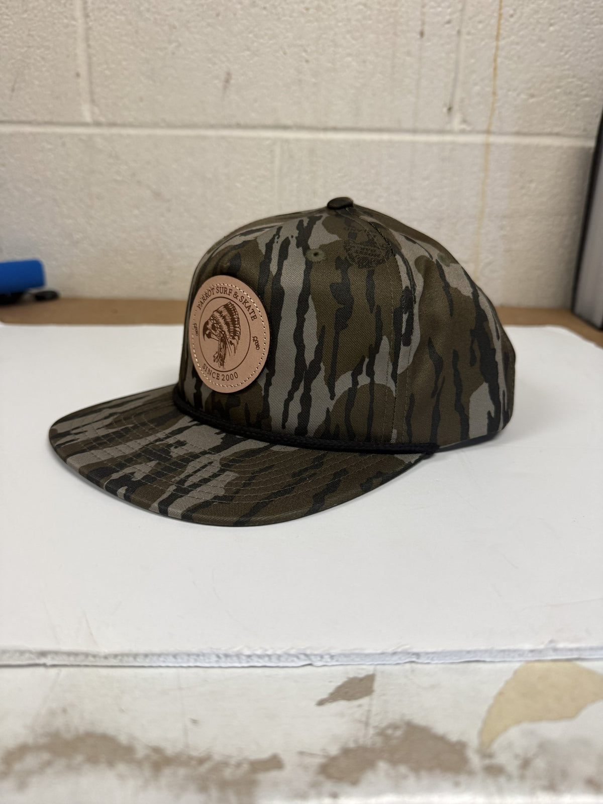 Parrot Surf & Skate 256P Indian Rope hat in Mossy Oak Bottomland with black rope and leather Indian patch, side view - Parrot gear