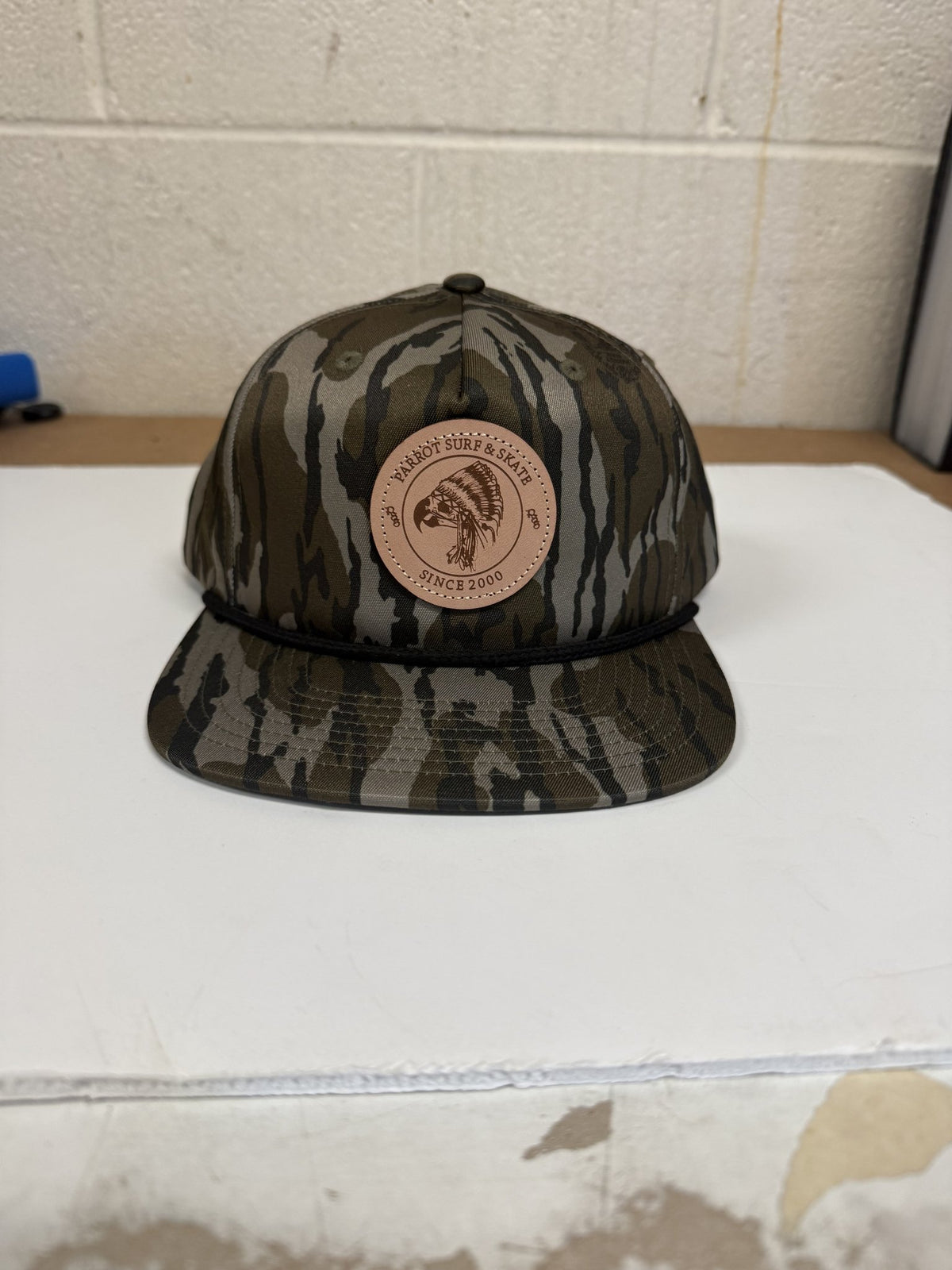 Parrot Surf & Skate 256P Indian Rope hat in Mossy Oak Bottomland with black rope and leather Indian patch, front view - Parrot gear